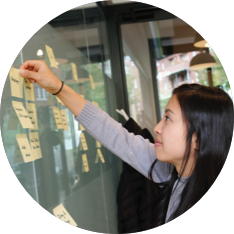 A woman pointing to sticky notes on a glass wall.